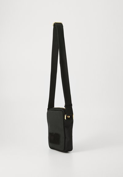 Geantă crossbody neagră cu o textură netedă, având un fermoar auriu și un buzunar frontal. Curea este ajustabilă și este din material textil.