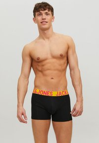 Schwarze Boxershorts mit einem gelben Bund, der pinke Schriftzüge zeigt. Der Stoff wirkt glatt und eng anliegend und präsentiert ein einfaches Design und Schnitt.