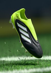 Neon yellow football boot with a black sole, three white stripes on the side, textured upper, and clear studded outsole for traction.