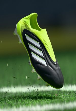 Neon yellow football boot with a black sole, three white stripes on the side, textured upper, and clear studded outsole for traction.