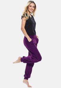 Top nero a maniche corte abbinato a pantaloni jogger viola larghi con tasche laterali e polsini arricciati. Tessuto morbido, design casual.