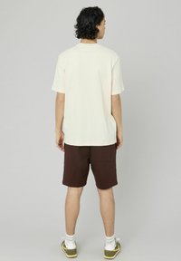 Chemise crème à manches courtes en tissu texturé, associée à un short marron. La tenue présente une coupe décontractée et un design minimaliste.