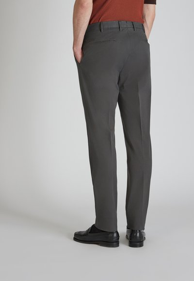 Pantaloni grigi su misura con una texture liscia, frontale piatto e tasche posteriori. Indossati con scarpe nere, mostrano un taglio dritto e una finitura curata.