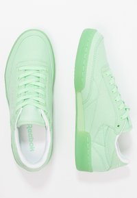 Ljusgröna kanvas sneakers med matchande snören och gummisulor. Har en logotyp på tungan och ett texturerat mönster på sidorna.