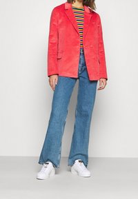 Korálový kordurový blazer s špičatými klopami, na dva knoflíky, spojený s pruhovanou košilí, rozšířenými modrými džíny a bílými teniskami.