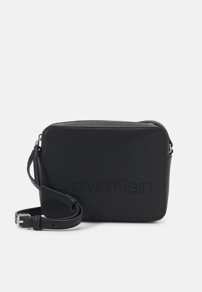 Sort læder skuldertaske med glat tekstur, rektangulær form og perforeret "Calvin Klein" logo på fronten. Justerbar rem medfølger.