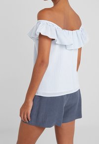 Blauw-wit gestreepte off-the-shoulder top met ruches mouwen, gemaakt van licht materiaal, gecombineerd met marineblauwe shorts.