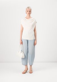 Weißes drapiertes Oberteil, hellblaue Denim-Jeans, beige Riemchensandalen und eine weiße Handtasche. Schlichtes Design, weicher Stoff und lässige Passform.