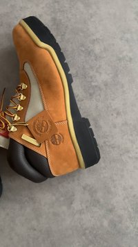 Botte de randonnée marron clair et marron avec semelle noire, lacets jaune-brun, et étiquettes indiquant qu'elle est imperméable et de qualité garantie.