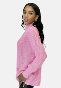 Maglione rosa a collo alto in maglia con maniche lunghe, caratterizzato da una vestibilità ampia e una texture a coste. Dettaglio notevole: collo alto e spacco laterale.