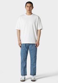 Hvit t-skjorte med kort erm og avslappet passform, kombinert med lyseblå, rette jeans og hvite joggesko. Minimalistisk design, uten mønstre.