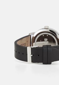 Correa de reloj de cuero negro con un cierre de metal plateado, que presenta una caja redonda y un fondo resistente al agua marcado con "5 BAR."