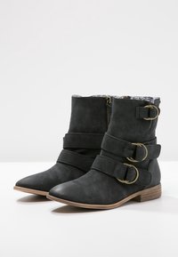 Černé kožené ankle boty s špičatou špičkou, plochým podpatkem a třemi ozdobnými přezkami. Interiér má vzorovanou podšívku.