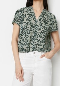Blouse à manches courtes en tissu léger, avec un fond vert et des motifs circulaires vert foncé, col en V et coupe décontractée.