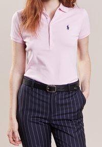 Rosa polo shirt med korta ärmar, med krage och tre knappar. Kombinerad med marinblå randiga byxor och ett svart läderbälte.