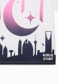 Camiseta blanca con un diseño de luna creciente y estrella en degradado de rosa a púrpura sobre un horizonte urbano negro. "ALHILAL" está impreso en árabe e inglés.