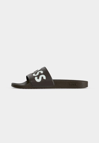 Une sandale slide marron foncé unique avec un logo blanc en relief "BOSS" sur la bride et une semelle texturée sur un fond uni clair.