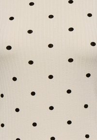Kremowy top o prążkowanej fakturze, ozdobiony czarnymi kropkami równomiernie rozmieszczonymi na tkaninie.