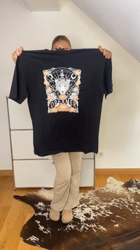 Musta puuvillapaita lyhyillä hihoilla, jossa on valkoinen ja oranssi graafinen kuvio leopardista, kukista ja sanasta "UNELMOI."
