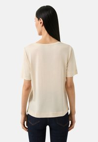Beige kortærmet skjorte med rund udskæring, glat tekstur, sideslids og løs pasform, båret med mørke denimbukser.