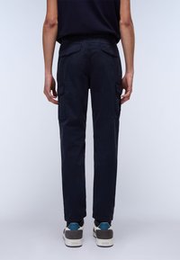 Navy cargo pants with a smooth texture, featuring dual side pockets and rear patch pockets, paired with white and grey sneakers.