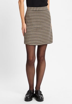 Schwarz-beige Hahnentritt-Minikleid mit einem taillierten Bund, A-Linien-Form und strukturiertem Stoff. Kombiniert mit schwarzen Slippern und transparenter Strumpfhose.