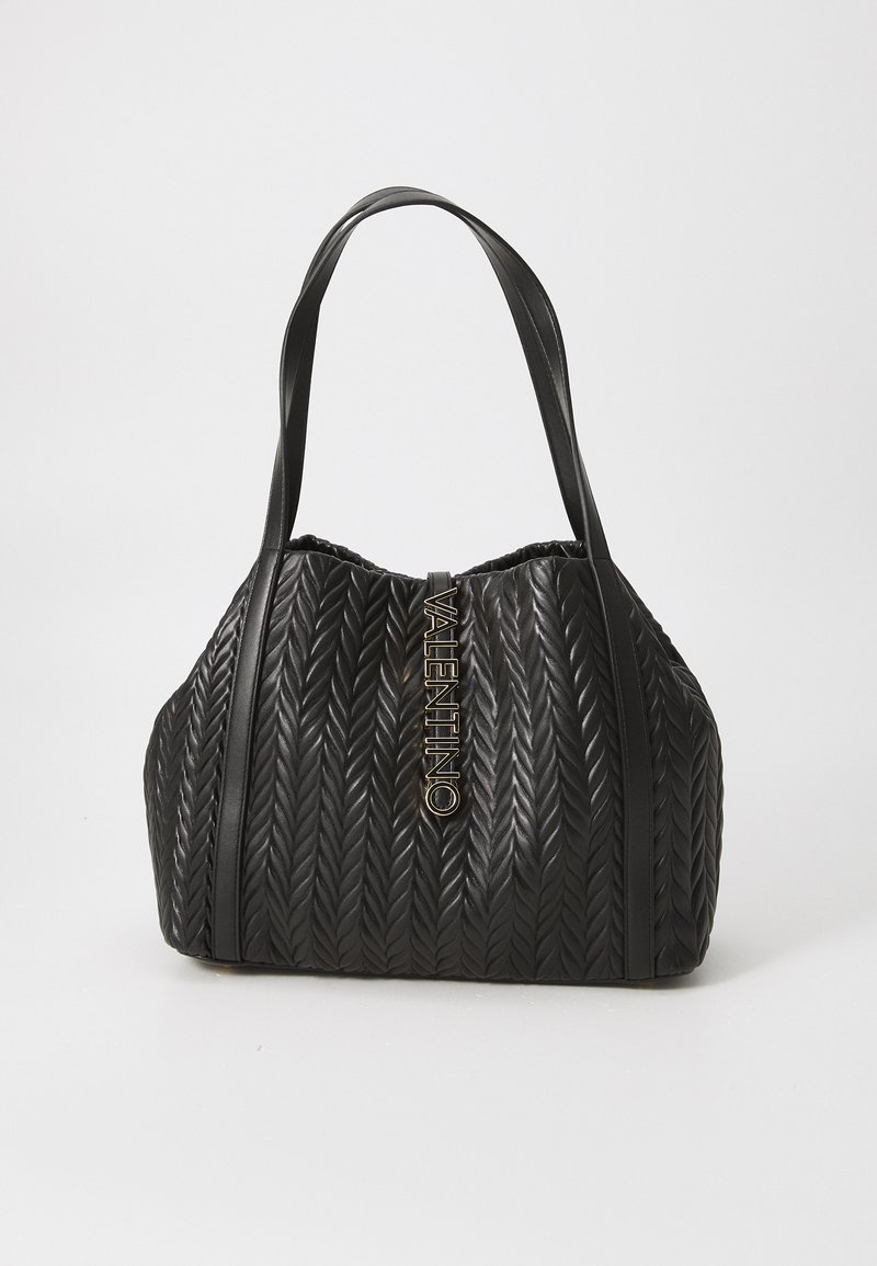 Črna prešita torbica v zaobljeni obliki, ki ima teksturiran vzorec tkanine, dvojne ročaje in izrazit zlat logotip.