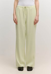 Lichtgroene, wijde broek met een elastische taille en trekkoord. Glad stofoppervlak, gedragen met donkere schoenen, weergegeven tegen een neutrale achtergrond.