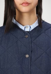 Gequilte denim vest in een donkere blauwtint, met een drukknoopsluiting en een lichtblauw overhemd eronder met kraag.