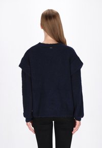 Marineblå sweater med en blød tekstur, løs pasform og drop-shoulder. Har ribbede manchetter og kant. Bagved udsigt viser enkelt design og logo tag.