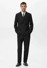 Schwarzer doppeltknopfiger Anzug mit taillierter Passform, mit gekerbten Revers und passenden schwarzen Dressschuhen. Ein knackig weißes Hemd und eine schwarze Krawatte runden den Look ab.