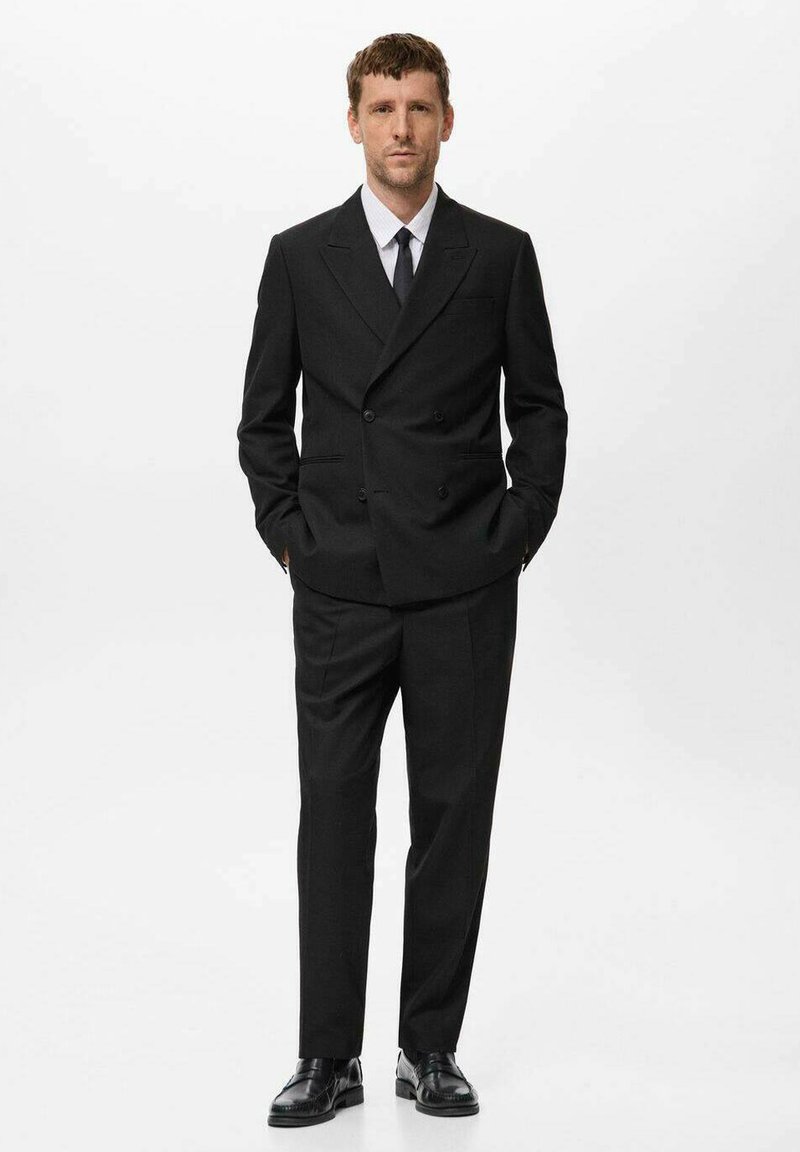 Schwarzer doppeltknopfiger Anzug mit taillierter Passform, mit gekerbten Revers und passenden schwarzen Dressschuhen. Ein knackig weißes Hemd und eine schwarze Krawatte runden den Look ab.