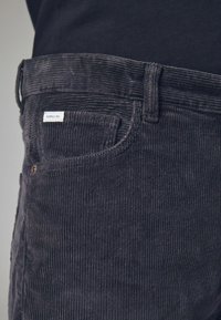 Mørkegrå kordfløjlsbukser med lodret ribbning, et klassisk fem-lomme design og et lille "SUPPLY CO." mærke nær livet.