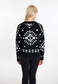 Maglione nero con motivi geometrici bianchi, tra cui diamanti e frecce, con una finitura in maglia testurizzata e pelosa.