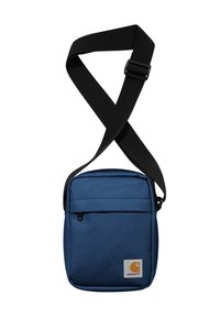 Bolso cruzado azul marino hecho de un tejido duradero, con un bolsillo frontal con cremallera y una correa negra ajustable. Logo de Carhartt visible.