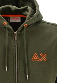 Felpa verde con zip, dotata di triangolo ricamato arancione e logo X sul petto, occhielli arancioni e etichetta di taglia "SUN68 M" all'interno del colletto.