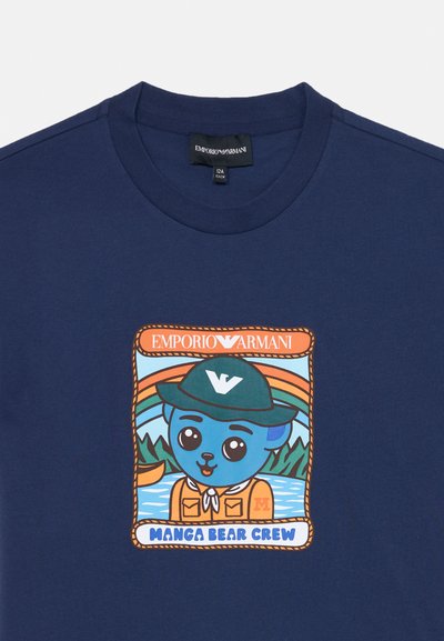 Granatowa koszula z kolorową naszywką przedstawiającą kreskówkowego niebieskiego misia w zielonym kapeluszu i pomarańczowej kurtce nad jeziorem, oznaczona napisem "Manga Bear Crew."