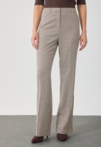 Pantalons à taille haute en plaid beige et marron avec une coupe évasée, fabriqués en tissu texturé, comportant des poches latérales et des plis repassés.