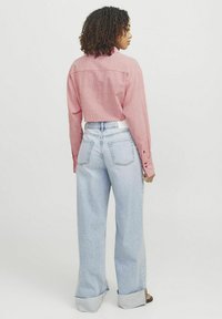 Rød- og hvidstribet cropped skjorte parret med lyseblå løse jeans med baglommer og frayed kant. Model set bagfra.