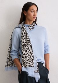 Jasnoniebieski kaszmirowy sweter z czarno-kremowym szalikiem w kwiatowy wzór, z frędzlami na krawędziach i miękką fakturą, noszony w swobodnym stylu.