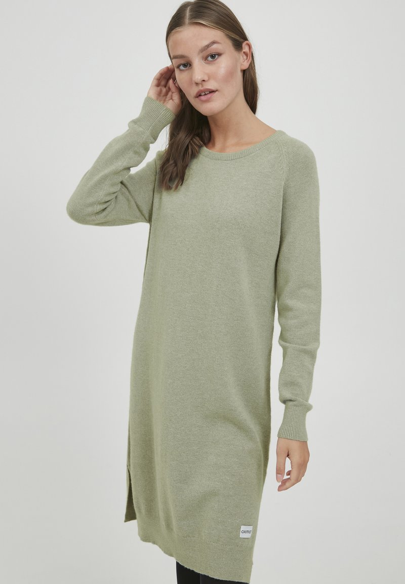 Abito lavorato a maglia verde chiaro con maniche lunghe, scollatura rotonda, spacco laterale e polsini a coste. Presenta un'etichetta all'orlo.