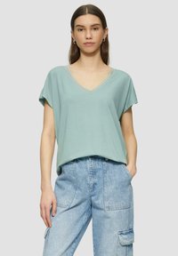 Lichtgroene V-hals T-shirt met korte mouwen, voorzien van kanten rand langs de halslijn, gecombineerd met lichtblauwe cargobroek. Zachte katoenen stof.