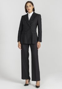 Czarny garnitur w paski z podwójnym żakietem i spodniami o szerokich nogawkach. Gładka faktura, dopasowany krój, z dwoma widocznymi kieszeniami z przodu.