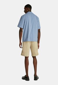 Camicia azzurro chiaro a maniche corte con colletto, abbinata a pantaloni corti beige, vista da dietro. Design semplice, materiale in cotone, dettagli minimi.