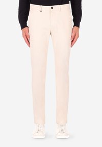 Pantaloni beige in cotone dalla vestibilità slim, con davanti piatto e design a cinque tasche, dotati di chiusura con bottone e texture sottile. Indossati con sneakers bianche.