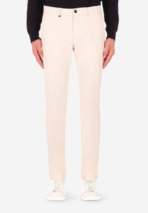 Pantaloni beige in cotone dalla vestibilità slim, con davanti piatto e design a cinque tasche, dotati di chiusura con bottone e texture sottile. Indossati con sneakers bianche.