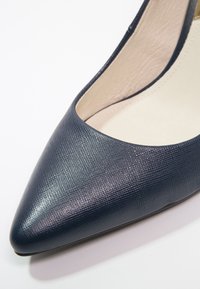 Chaussure pour femme en cuir texturé bleu marine à bout pointu avec doublure intérieure beige rembourrée sur fond blanc.