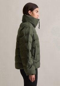 Veste rembourrée olive avec un col haut, fermeture éclair et poches latérales. Présente un design matelassé et une texture lisse.
