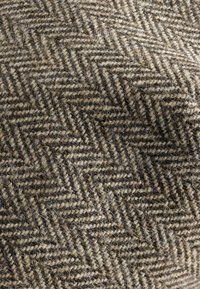 Hounds-tooth mönstrad tyg i bruna och beige nyanser, med en texturerad ullkomposition. Närbild visar den intrikata vävningen.