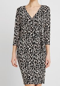 Robe imprimée léopard noir et beige avec un design cache-cœur, un col en V et des manches trois-quarts, fabriquée dans un tissu lisse. Dispose d'un détail noué.
